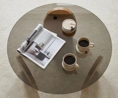 Round glass coffee table with two cups of coffee and a magazine on a light-colored floor.
