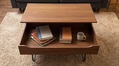 Wooden coffee table with an open drawer containing books and a mug, on a beige carpet.